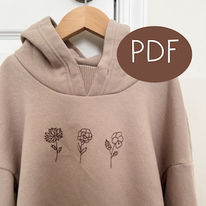 May include: A beige hoodie with a brown embroidered design of three flowers on the front. The hoodie has a hood and a drawstring. The text "PDF" is on a brown circle in the upper right corner of the image.