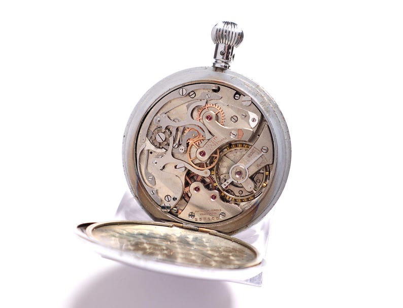 May include: A silver pocket watch with an open face, revealing the intricate mechanical workings of the timepiece. The watch's gears, springs, and other components are visible, showcasing the craftsmanship. The watch is set against a white background.
