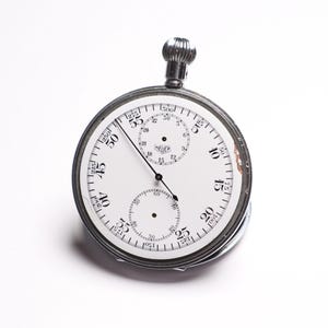 May include: A vintage Heuer stopwatch with a white face and black numerals. The stopwatch has a silver metal casing and a winding crown at the top. The face includes three sub-dials and the Heuer logo. The hands are black.