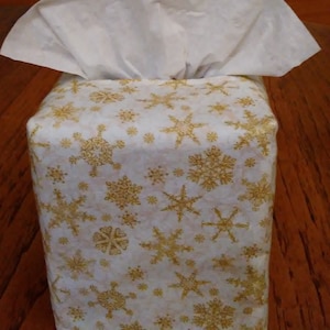 May include: A white tissue box cover with a gold snowflake pattern.