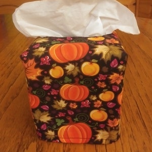 May include: A tissue box cover with a black background and a pattern of orange pumpkins, green leaves, and red berries.