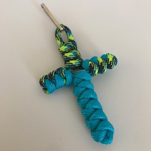 May include: A turquoise and black paracord keychain with a silver clip. The keychain is braided in a cross shape.