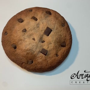 Peut inclure: Un grand cookie rond aux pépites de chocolat avec un extérieur brun légèrement brûlé et de nombreuses pépites de chocolat sur le dessus.