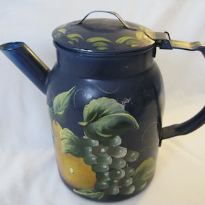 May include: A navy blue enamelware teapot with a lid and handle. The teapot is decorated with hand-painted yellow pears, green grapes, and leaves. The spout and handle are dark blue.