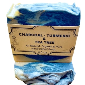 May include: Two bars of handmade soap, one on top of the other. The top bar is blue and yellow with a brown label that reads "CHARCOAL - TURMERIC & TEA TREE. All Natural, Organic & Pure Handcrafted Soap. 4.0 oz."