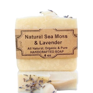 May include: Two bars of handcrafted soap, stacked. The top bar has a brown label that reads "Natural Sea Moss & Lavender." The bottom bar has lavender buds on top. The soap is 4 oz.