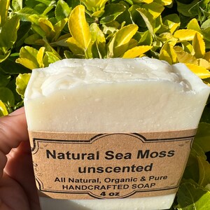 May include: A white bar of soap with a brown label that reads "Natural Sea Moss unscented All Natural, Organic & Pure HANDCRAFTED SOAP 4 oz".