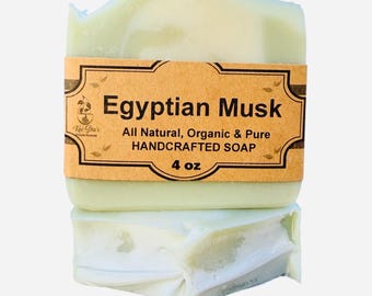 Puede incluir: Una pastilla de jabón rectangular de color verde pálido envuelta en una etiqueta de papel color canela. La etiqueta muestra el texto Egyptian Musk, All Natural, Organic & Pure HANDCRAFTED SOAP, 4 oz y el logo de Kai-Sha's Organic Products.