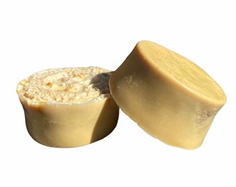 May include: Two round bars of natural soap, one is cut in half to show the inside. The soap is a light beige color.