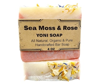 May include: A bar of handcrafted soap with a brown label that reads "Sea Moss & Rose YONI SOAP All Natural, Organic & Pure Handcrafted Bar Soap 4 OZ". The soap is pink and white with dried flowers on top.