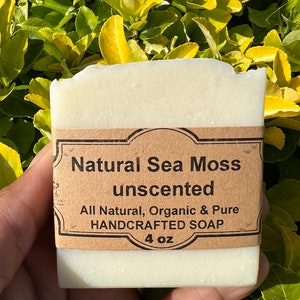 May include: A white bar of soap with a brown label that reads "Natural Sea Moss unscented All Natural, Organic & Pure HANDCRAFTED SOAP 4 oz".