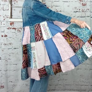 Blue denim coat with three tiers of fabric added to the bottom. Pinks, blues and brown fabrics on bottom. Hits past the knees.