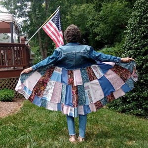 Blue denim coat with three tiers of fabric added to the bottom. Pinks, blues and brown fabrics on bottom. Hits past the knees.