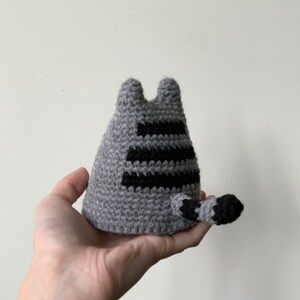 Puede incluir: Juguete de gato de crochet gris con rayas negras en la espalda y una cola.