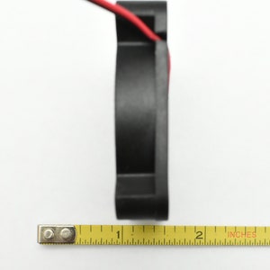May include: A black computer fan with red wires, measured with a yellow tape measure that reads "1" and "2" inches.
