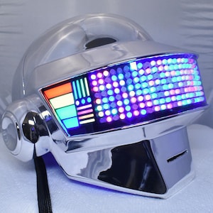 May include: A shiny chrome helmet featuring a curved visor embedded with a grid of multicolored LED lights. The display shows a vibrant array of blue, purple, and pink dots, with a side panel displaying vertical bars in orange, yellow, and green.