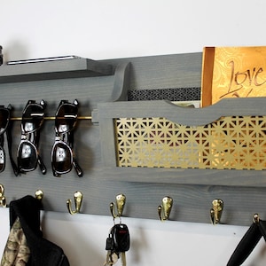 May include: A gray wooden wall organizer with a shelf, a mail slot, a sunglasses holder, and hooks. The mail slot has a gold metal mesh insert. The organizer has the word "Love" written on a piece of paper in the mail slot.