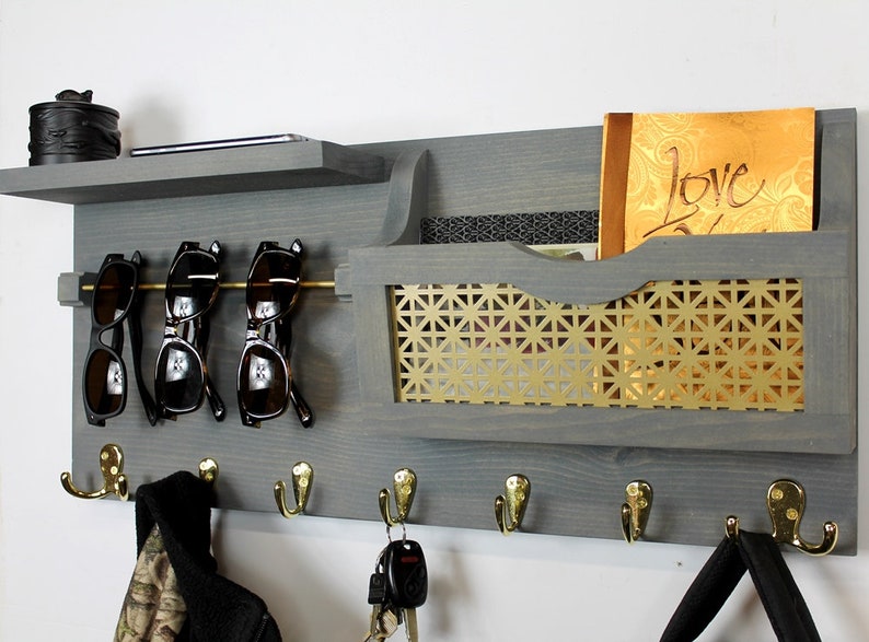 May include: A gray wooden wall organizer with a shelf, a mail slot, a sunglasses holder, and hooks. The mail slot has a gold metal mesh insert. The organizer has the word "Love" written on a piece of paper in the mail slot.