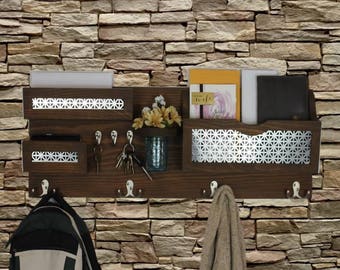 May include: A brown wooden wall organizer with a key holder, two shelves, and a mail slot. The organizer has a silver metal mesh design on the front. The organizer is mounted on a stone wall.