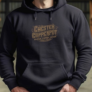 Könnte beinhalten: Schwarzer Kapuzenpullover mit einem goldenen Logo, auf dem "Chester Copperpot Guided Caving Tours Astoria Oregon" steht.