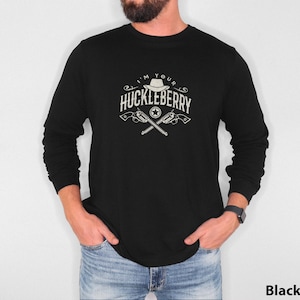 Puede incluir: Camiseta negra de manga larga con un diseño gráfico blanco que dice "I'm Your Huckleberry" con un sombrero de vaquero y pistolas cruzadas.