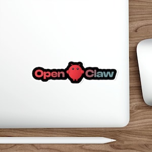 Pode incluir: Um autocolante com o texto "Open Claw" em contorno preto, com uma personagem de desenho animado vermelha no centro. O autocolante está numa superfície branca, com um fundo de madeira.