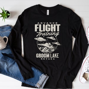 Puede incluir: Camiseta negra de manga larga con un gráfico de estilo vintage de un OVNI y el texto "Advance Flight Training Groom Lake Nevada".