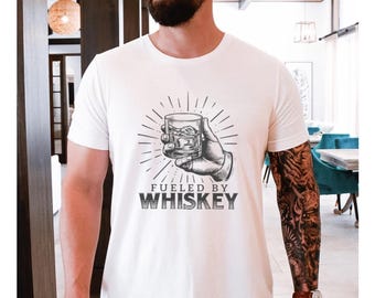 Könnte beinhalten: Weißes T-Shirt mit einer Grafik einer Hand, die ein Glas Whisky hält, mit dem Text "Fueled by Whiskey".