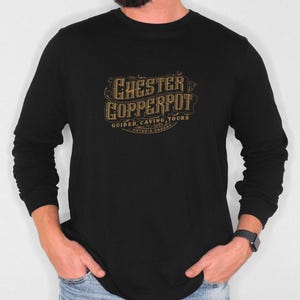 Puede incluir: Camiseta negra de manga larga con un gráfico dorado del texto "Chester Copperpot Guided Caving Tours Astoria, Oregon".
