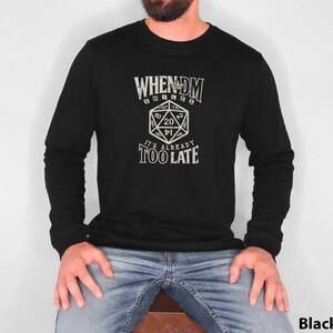 Op de afbeelding: Zwart longsleeve shirt met een witte afbeelding van een dobbelsteen en de tekst "When the DM rolls a 20, it's already too late."