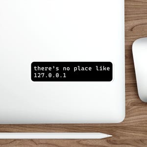 Könnte beinhalten: Ein schwarzer Aufkleber mit weißem Text, der "there's no place like 127.0.0.1" lautet. Der Aufkleber ist rechteckig mit abgerundeten Ecken und befindet sich auf einem weißen Laptop.