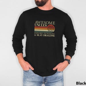 May include: Black long-sleeve t-shirt with a vintage-style graphic that reads "Awesome Uncles Explore Dungeons & Slay Dragons". The graphic features a rainbow stripe and a Dungeons & Dragons dice.