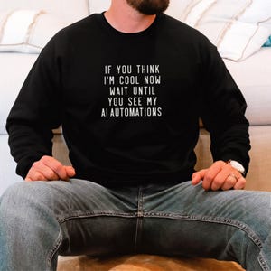 Op de afbeelding: Een zwart sweatshirt met de tekst "If you think I'm cool now wait until you see my AI automations" in wit gedrukt.