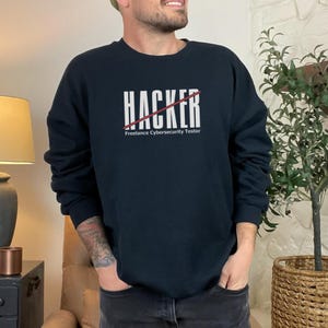 May include: A black sweatshirt with a white graphic that says "HACKER" with a red line through it. The text below the graphic says "Freelance Cybersecurity Tester".