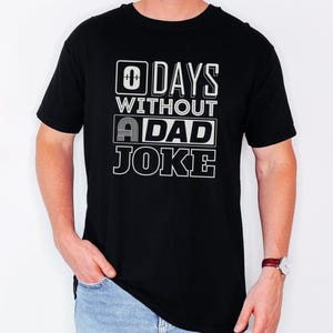 May include: Black t-shirt with a white graphic that says "0 Days Without A Dad Joke".
