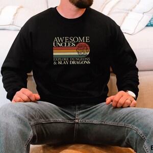 May include: Black sweatshirt with the text "AWESOME UNCLES EXPLORE DUNGEONS & SLAY DRAGONS" in a retro design. The graphic includes a colorful striped background and a Dungeons & Dragons-style die. The sweatshirt is a crew neck.