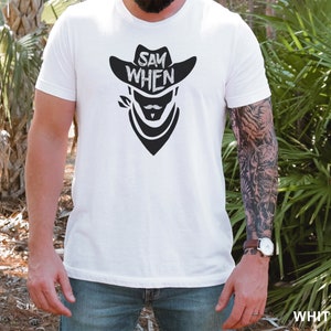 May include: White t-shirt with a black graphic of a cowboy wearing a hat and bandana with the text "Say When".