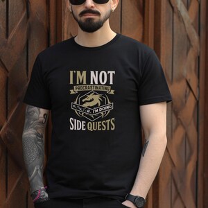 Puede incluir: Camiseta negra con un gráfico dorado de un dragón y el texto "No estoy procrastinando, estoy haciendo misiones secundarias."