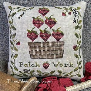 May include: A cross-stitched pillow with a basket of strawberries. The strawberries are red with green tops, and the basket is brown. The words "Patch Work" are stitched below the basket, with green vines and a spider web design.