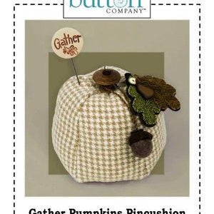 May include: A brown and white plaid pumpkin pincushion with a green felt leaf and a brown felt acorn. The pincushion has a wooden button on top and a small wooden sign that says "Gather". The text "Gather Pumpkins Pincushion" is printed below the image. The text "Add a wooly pumpkin to your Autumn sewing room. Instructions are included for the Gather Acorns fob. P1059" is printed below the title.