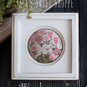 May include: A white framed cross-stitch sampler with a white sheep surrounded by pink flowers and green leaves. The title of the sampler is "Woolemina" and the artist is credited as Paulette Stewart.