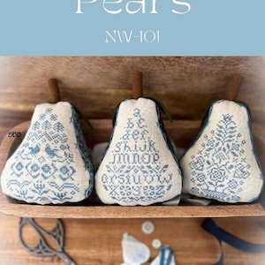 May include: Three blue and white embroidered pear-shaped pillows with a blue and white floral design. The pillows are sitting on a wooden shelf with a blue ribbon and buttons. The text "Bluework Pears NW-101" is at the top of the image. The image also includes a logo for Annie Beez Softie.