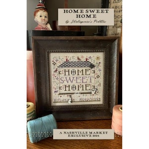 May include: A framed cross-stitch sampler with the text "HOME SWEET HOME" in a vintage style. The sampler is surrounded by a dark brown frame and is displayed on a wooden surface. The text "A NASHVILLE MARKET EXCLUSIVE 2021" is printed below the frame.