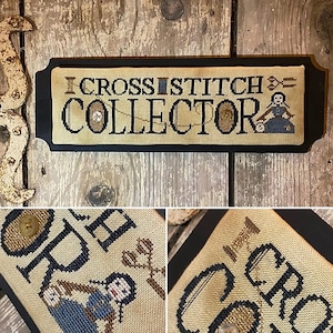 May include: A cross stitch sampler with a black frame and the text "I Cross Stitch Collector" in white. The sampler features a small cross stitch design of a woman with a spool of thread and scissors.