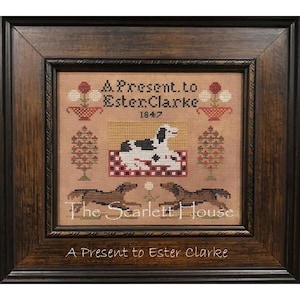 May include: A framed cross-stitch sampler with a brown wooden frame. The sampler features a dog, two horses, and a floral design. The text "A Present to Ester Clarke 1847" is stitched in the center of the sampler. The text "The Scarlett House" is stitched below the design.