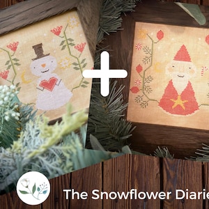 May include: Two framed cross-stitch patterns, one featuring a snowman holding a heart and the other a red-robed figure with a star. The frames are brown wood and the background is a rustic wooden surface. The text "The Snowflower Diaries" is below the frames.