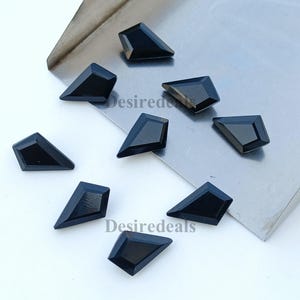 May include: A selection of black, kite-shaped gemstones with multiple facets. The gemstones are displayed on a silver surface, with the word "Desiredeals" visible. The gemstones have a polished, reflective surface.