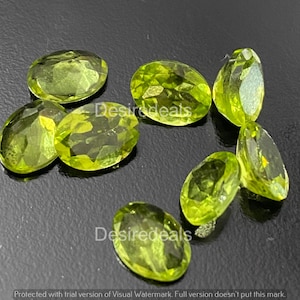 Può includere: Una collezione di pietre preziose di peridoto verde chiaro, taglio ovale. Le pietre sfaccettate sono disposte su una superficie scura, mostrando la loro chiarezza e il colore vibrante. Include il testo "Desiredeals".