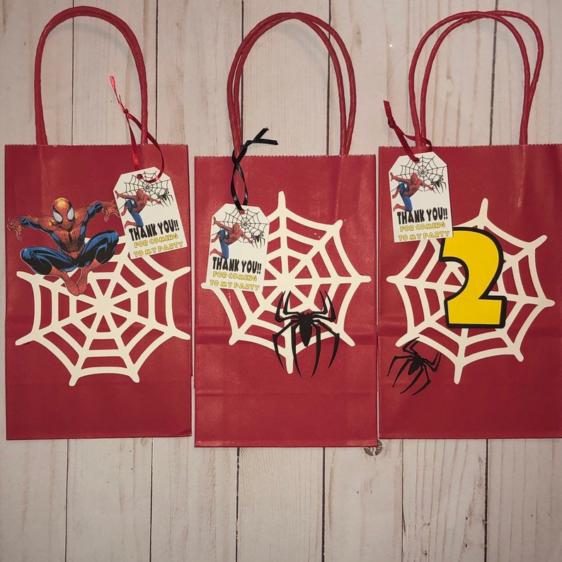 May include: Three red gift bags with white spider web designs and a Spiderman character. Each bag has a tag that says "Thank You!! For coming to my party".