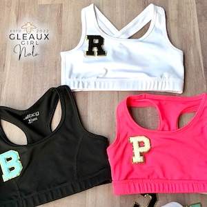 Könnte beinhalten: Drei Sport-BHs in verschiedenen Farben mit Buchstaben darauf. Der erste BH ist weiß mit einem schwarzen Buchstaben "R" darauf. Der zweite BH ist schwarz mit einem hellblauen Buchstaben "B" darauf. Der dritte BH ist pink mit einem weißen Buchstaben "P" darauf.